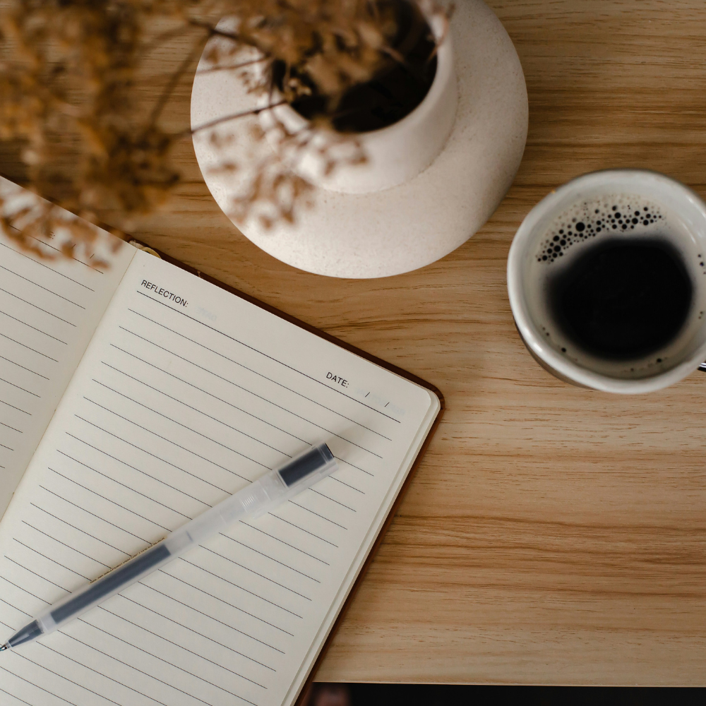 Open journal with pen and coffee cup on a wooden table, soft natural light